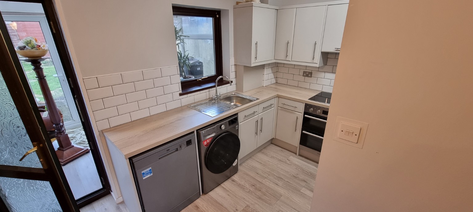 Long light wood-effect worktop with stainless steel sink and grey appliances beneath