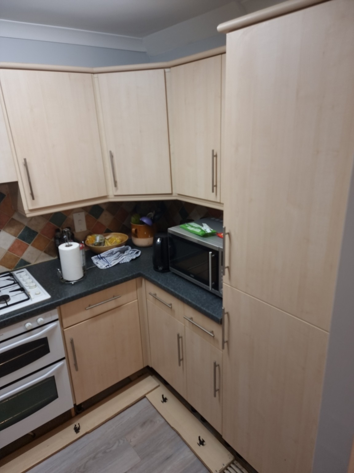 Original pale wood-effect kitchen doors and tall unit beside dark worktops